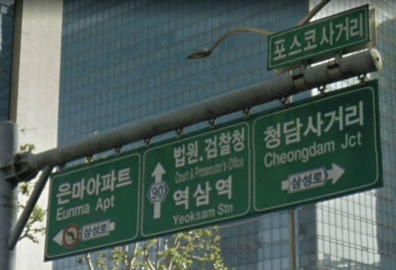 서울 테헤란로 교차로 표지판 근접. 은마아파트, 포스코사거리, 역삼역이 크게 적혀 있고 삼성로는 작은 화살표로만 표기되어 있다.